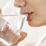 Chica tomando agua de un vaso de vidrio