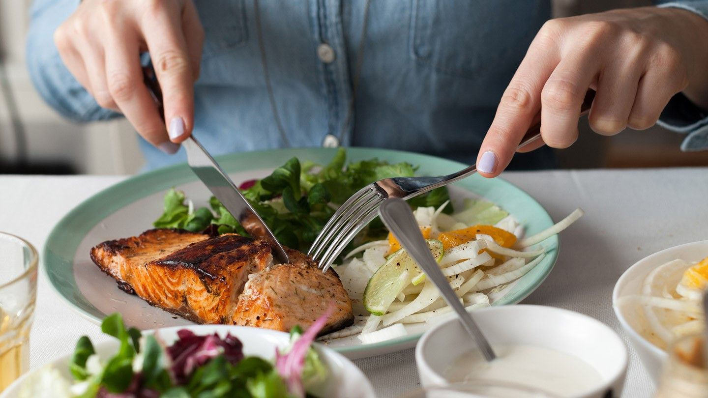 Mujer comiendo los alimentos en un plato con salmón y verduras