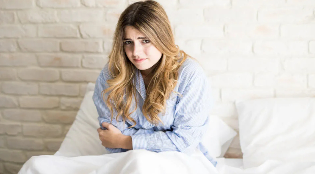 chica en la cama con dolor de estomago