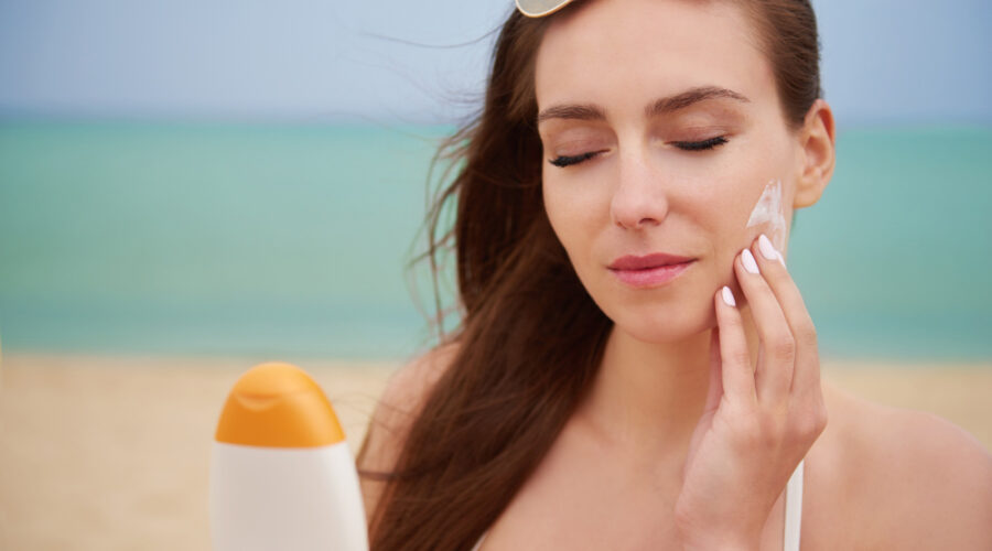 Una mujer aplicándose protector solar en la playa con un fondo soleado.